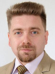 Portrait Dmytro S. Inosov mit blonden, aufgestylten Haaren, Bart und hellem Sakko vor hellem Hintergrund.